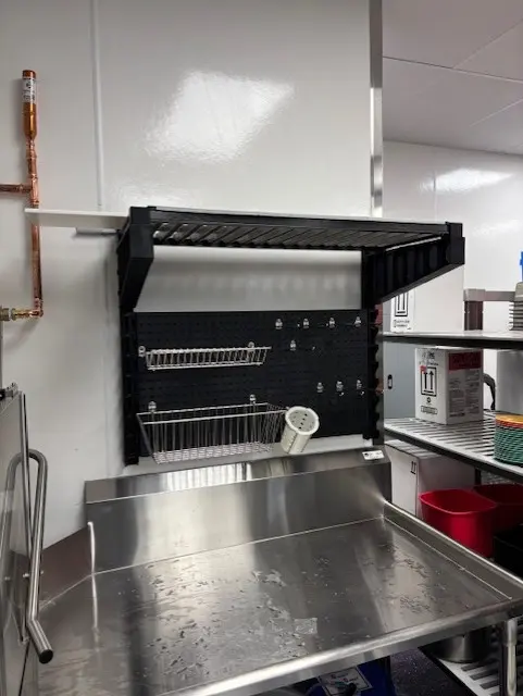 Wall shelving and pegboard installed above a stainless sink