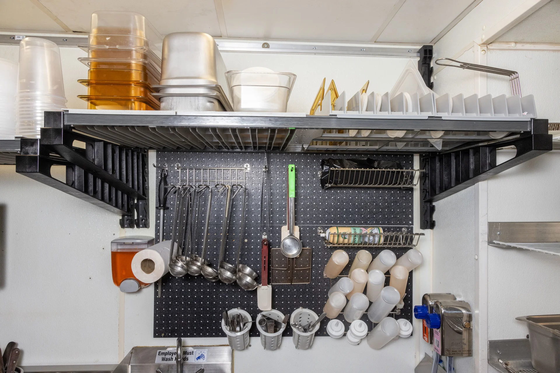 Elevation wall shelving with food containers and a utensil pegboard above a sink at Rouge Island