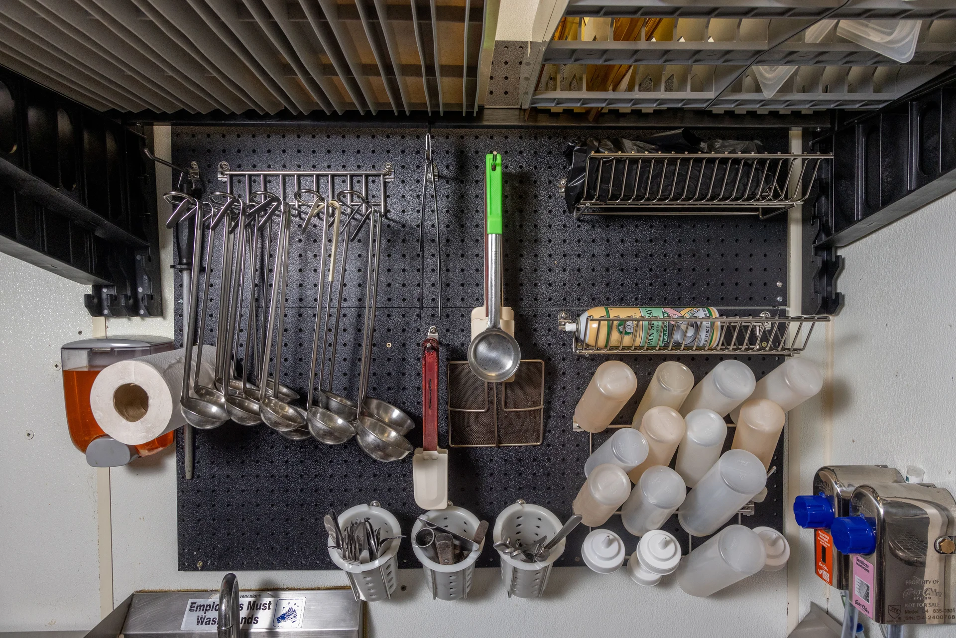 Close-up of ladles, utensils, and squeeze bottles organized on a wall-mounted pegboard at Rouge Island