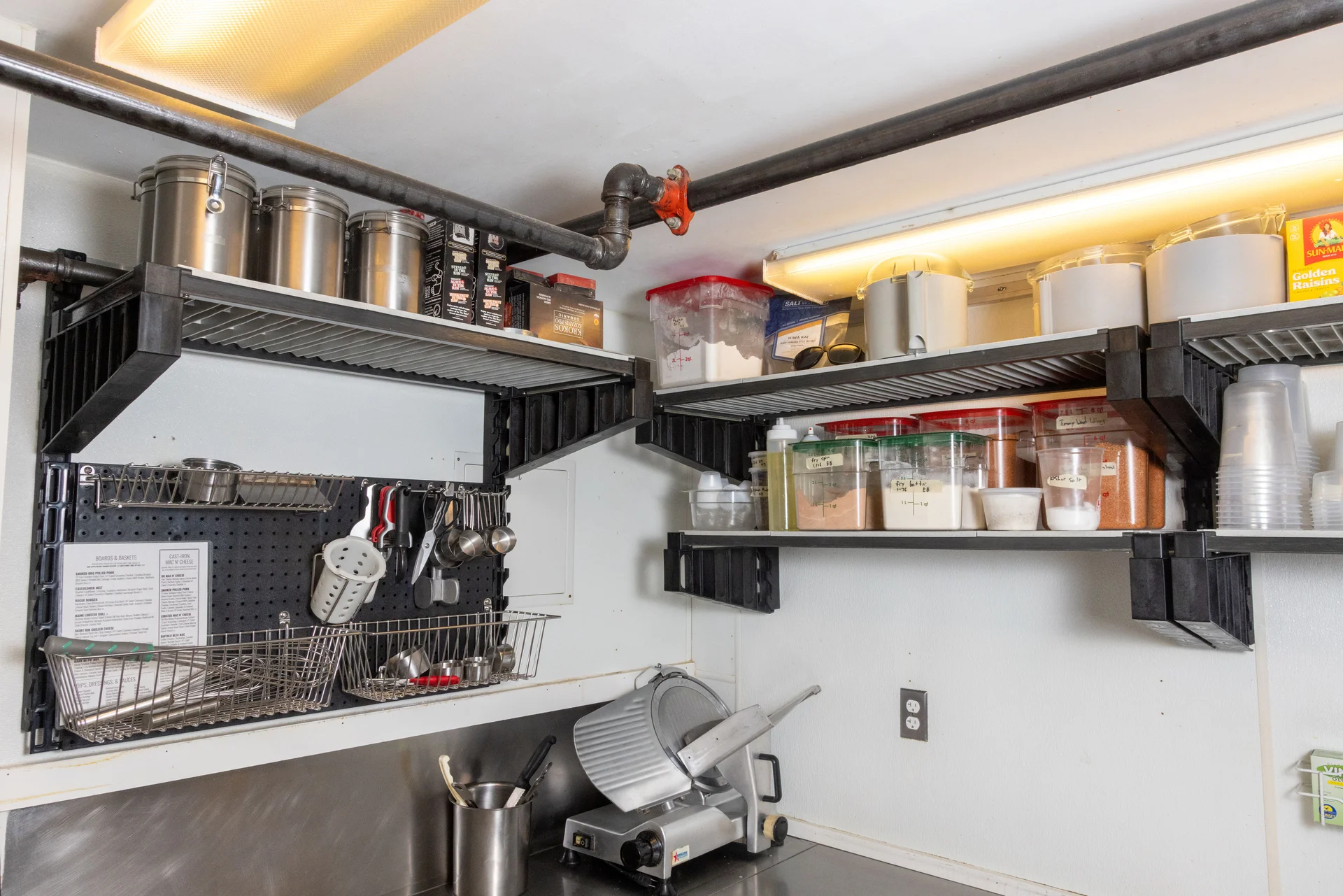 Corner wall shelving with ingredient containers and kitchen tools above a prep counter at Rouge Island